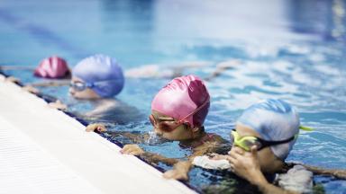 Image de quatre enfants avec des bonnets de bain et lunettes de plongée au bord d'une piscine